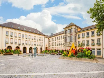 Im Zentrum des Bildes steht ein gepflasterter Platz mit Brunnen und herum Planzenbete. Hinten dran ist das Rathaus von Frankenthal zu sehen.