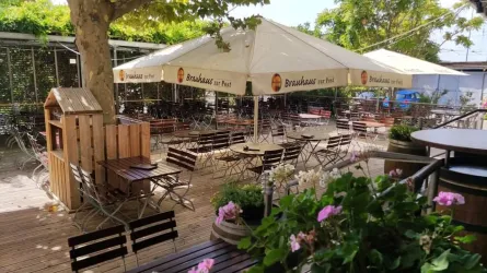 Eine einladende Terrasse mit Holzstühlen und Schirmen. Überall blühen Blumen und es gibt viel Platz zum Entspannen.