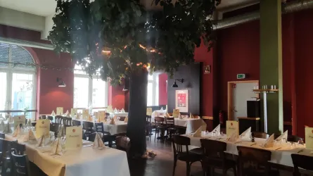 Ein elegantes Restaurant mit Holzstühlen und Tischen, die für Gäste gedeckt sind. In der Mitte steht ein großer Baum, der eine gemütliche Atmosphäre schafft.