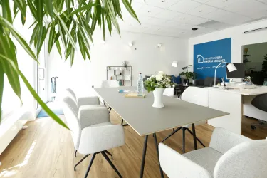 Ein modern gestalteter Büroraum mit einem großen Tisch und bequemen Stühlen. Pflanzen und dekorative Elemente schaffen eine einladende Atmosphäre.