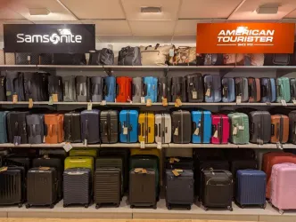 Ein Regal mit einer Vielzahl von Koffern verschiedener Farben und Größen. Die Marken "Samsonite" und "American Tourister" sind gut sichtbar.