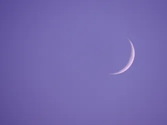 Eine schmale Mondsichel steht vor einem lila Himmel. Die Atmosphäre wirkt ruhig und friedlich.