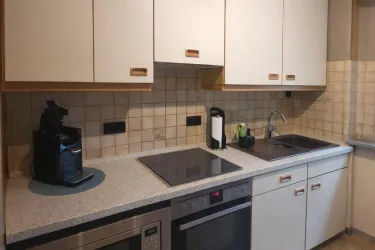 Eine moderne Küche mit hellen Schränken und einem Arbeitsbereich aus Granit. Dazu gehören Kochfeld, Spüle und Kaffeemaschine.
