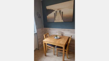 Ein gemütlicher Essbereich mit einem Holztisch und zwei Stühlen. An der Wand hängt ein Bild mit einer ruhigen Landschaft.