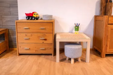 Ein helles Zimmer mit einem Holzschrank und einem kleinen Tisch. Auf dem Tisch stehen Buntstifte und ein Spielzeugauto auf dem Schrank.