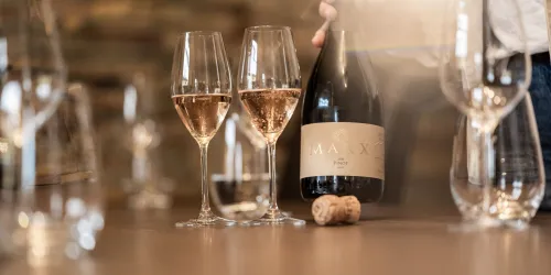 Eine Flasche Roséwein wird in zwei Gläser gegossen. Der Tisch ist mit weiteren Gläsern und einem Korken dekoriert.