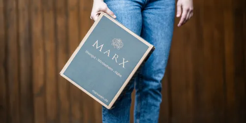 Eine Person hält eine elegante Box mit der Aufschrift „MARX“. Die Box hat eine grüne Stoffoberfläche und sieht hochwertig aus.