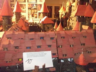 Ein detailliertes Modell eines mittelalterlichen Dorfes mit roten Dächern und Türmen. Im Vordergrund ist eine erläuternde Beschriftung zu sehen.