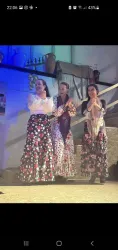 Drei Tänzerinnen in traditionellen bunten Trachten stehen auf der Bühne. Sie tanzen und lächeln, umgeben von stimmungsvollem Licht.