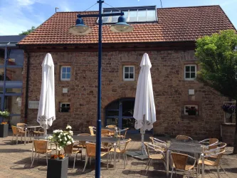 Ein schönes Café mit einer gemütlichen Außenfläche. Es gibt Tische mit Stühlen und Sonnenschirmen vor einer alten, steinernen Fassade.