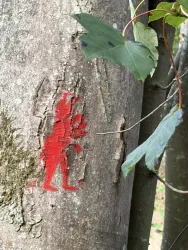 Ein roter Umriss einer Figur auf einem Baumstamm. Um die Figur wachsen grüne Blätter.