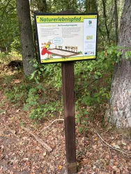 Ein Informationsschild über den Naturerlebnisweg im Wald. Es enthält Hinweise zu den Tierarten und der Umgebung.