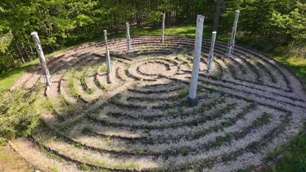 Ein labyrinthartiger Garten mit Wegführungen aus Steinen und Pflanzen. In der Mitte stehen mehrere Säulen zwischen den grünen Beeten.