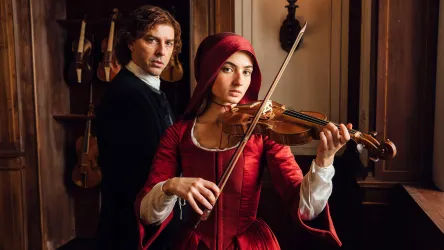 Eine Frau in einem roten Kleid spielt Geige, während ein Mann hinter ihr steht. Die Atmosphäre ist nostalgisch und elegant.