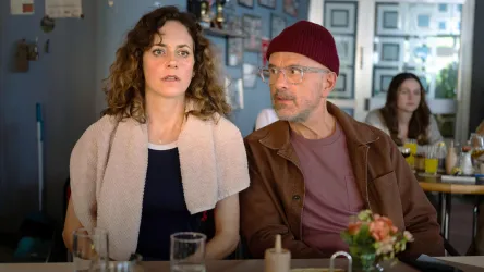 Zwei Personen sitzen in einem Café. Die Frau hat einen nachdenklichen Ausdruck, während der Mann sie ansieht.