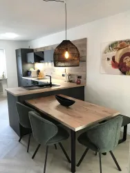 Eine moderne Küche mit einer Holzarbeitsplatte und stilvollen Stühlen. Eine hängende Lampe sorgt für eine gemütliche Atmosphäre.