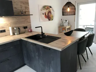 Eine moderne Küche mit einer stylishen Kücheninsel und einem schwarzen Spülbecken. Der Raum ist hell und freundlich, mit einem Esstisch und bequemen Stühlen.