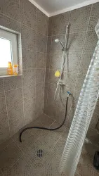 Eine moderne Dusche mit beige-fliesen und einer Duscheinstellung. Auf dem Fensterbrett stehen einige Pflegeprodukte.