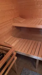 Eine Holzsauna mit zwei Bänken und warmem Ambiente. Der Raum ist einfach und einladend gestaltet.