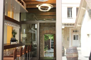 Ein modernes Café mit Holz- und Glaselementen. Im Hintergrund sind alkoholische Fässer und ein gewölbter Eingang sichtbar.