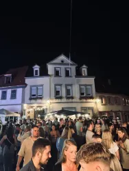 Eine lebhafte Menschenmenge versammelt sich nachts vor einem Gebäude. Die Atmosphäre ist festlich und einladend.