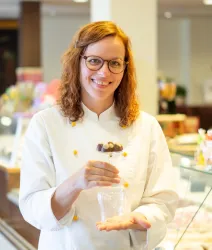 Susanne Bäcker-Valerius mit Pralinen auf einem Weinglas vor einer Kuchen/Pralinentheke