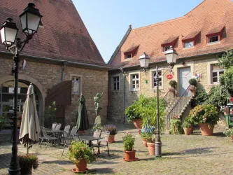 Ein malerischer Innenhof mit Steinen und Pflanzen. Rund um den Hof befinden sich Sitzgelegenheiten und laternen.