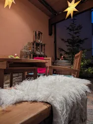 Eine gemütliche Terrasse mit einem Holztisch und Stühlen, dekoriert mit leuchtenden Sternen. Im Hintergrund steht eine Pflanze und einige Kerzen sorgen für eine warme Atmosphäre.