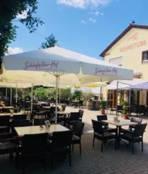 Eine Terrasse mit Tischen und Stühlen unter großen Sonnenschirmen. Im Hintergrund ist ein Gebäude mit dem Schriftzug "WEINSTUBE" zu sehen.