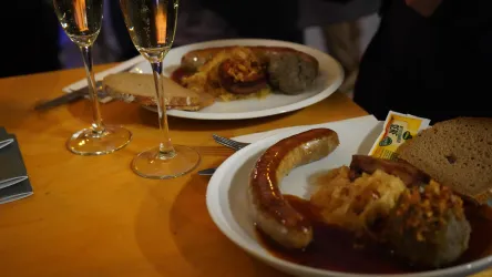 Ein Teller mit Wurst und Sauerkraut, begleitet von Brot. Im Hintergrund stehen zwei Gläser Sekt.