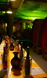 Eine geschmackvolle Weinprobe mit dekorierten Flaschen auf einem langen Tisch. Im Hintergrund sind große Weinfässer und sanfte grüne Beleuchtung zu sehen.