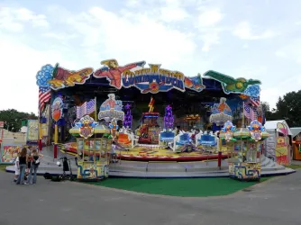 Ein farbenfroher Jahrmarkt mit einem Karussell namens "Commander". Viele Lichter und ein festliches Ambiente laden zum Spaß ein.