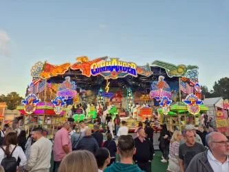 Ein belebter Jahrmarkt mit vielen bunten Lichtern und Attraktionen. Menschen genießen die Atmosphäre und die Fahrgeschäfte.