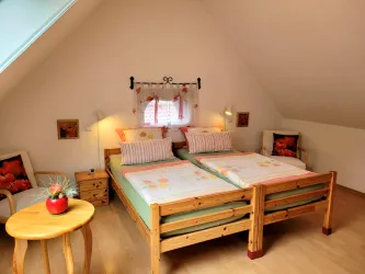 Ein gemütliches Schlafzimmer mit zwei Einzelbetten aus Holz. Die Wände sind hell gestrichen und es gibt dekorative Elemente wie Kissen und Bilder.