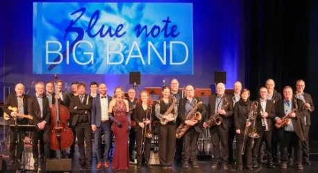 Eine Big Band steht auf der Bühne mit verschiedenen Instrumenten. Im Hintergrund leuchtet ein Banner mit dem Schriftzug "Blue Note BIG BAND".