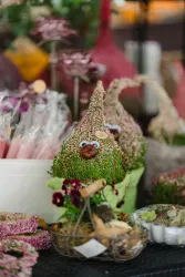 Bunte Pflanzenarrangements in verschiedenen Formen, darunter ein niedlicher dekorativer Kopf. Im Hintergrund sind viele weitere florale Dekorationen zu sehen.