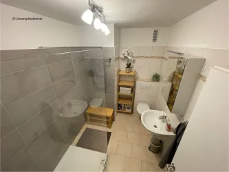 Ein modernes Badezimmer mit einer Dusche, einem Waschbecken und einem großen Spiegel. Die Wände sind in hellen Farbtönen mit einem eleganten Fliesendesign.