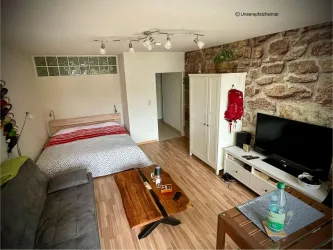 Ein modernes Zimmer mit einem Doppelbett, einer Couch und einem TV-Schrank. Die Wände sind elegant mit Steinen gestaltet, und die Einrichtung ist schlicht und einladend.