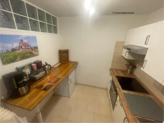Eine moderne Küche mit hellen Schränken und Holzarbeitsflächen. An der Wand hängt ein Bild von einem Leuchtturm.