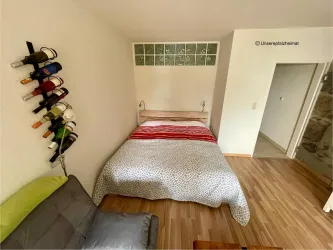 Ein gemütliches Schlafzimmer mit einem Doppelbett und einem farbigen Bettbezug. An der Wand ist ein Weinfass für Flaschen und ein kleiner Sessel ist sichtbar.