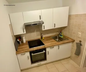 Eine moderne Küche mit weißen Schränken und Holzarbeitsplatte. Sie verfügt über einen Herd, eine Spüle und einen Backofen.