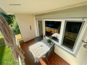Ein gemütlicher Balkon mit einem Tisch und Stühlen. Der Tisch ist mit einer Tischdecke bedeckt und es gibt Pflanzen auf dem Tisch.