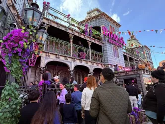 Ein geschäftiges Restaurant mit einer bunten Fassade und vielen Blumen. Menschen stehen davor und genießen die festliche Atmosphäre.