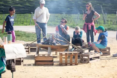 Eine Gruppe von Menschen sitzt um ein Feuer in der Natur. Sie genießen die Zeit miteinander und wirken entspannt.