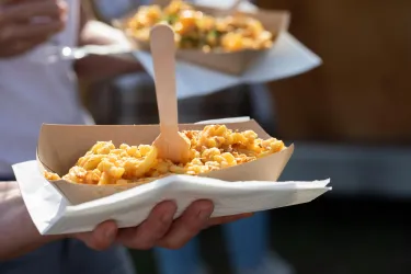 Ein handgehaltenes Schälchen mit frisch zubereiteten Nudeln. Daneben sind weitere Gerichte sichtbar.