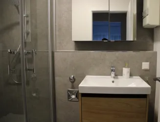 Ein modernes Badezimmer mit Dusche und einem weißen Waschbecken. Die Wände sind in Grautönen gehalten, und ein großer Spiegel hängt darüber.