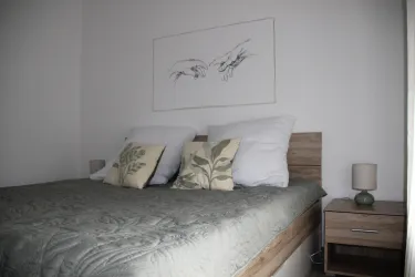 Ein gemütliches Schlafzimmer mit einem großen Bett und dekorativen Kissen. An der Wand hängt eine Zeichnung von Händen.