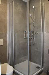 Eine moderne Dusche mit gläsernen Wänden und einer Handbrause. Der Boden ist gefliest und die Wände sind in neutralen Grautönen gehalten.