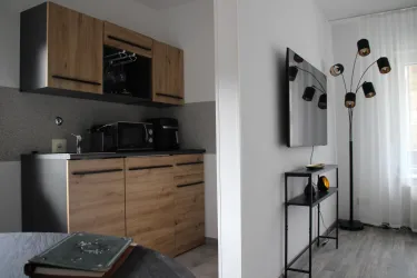 Eine moderne Küchenzeile mit Holzfronten und Küchengeräten. Im Hintergrund befindet sich ein Fernseher und ein eleganter Stehlampe.