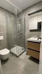 Ein modernes Badezimmer in neutralen Farben. Es enthält eine Duschkabine, ein Waschbecken und eine Toilette.